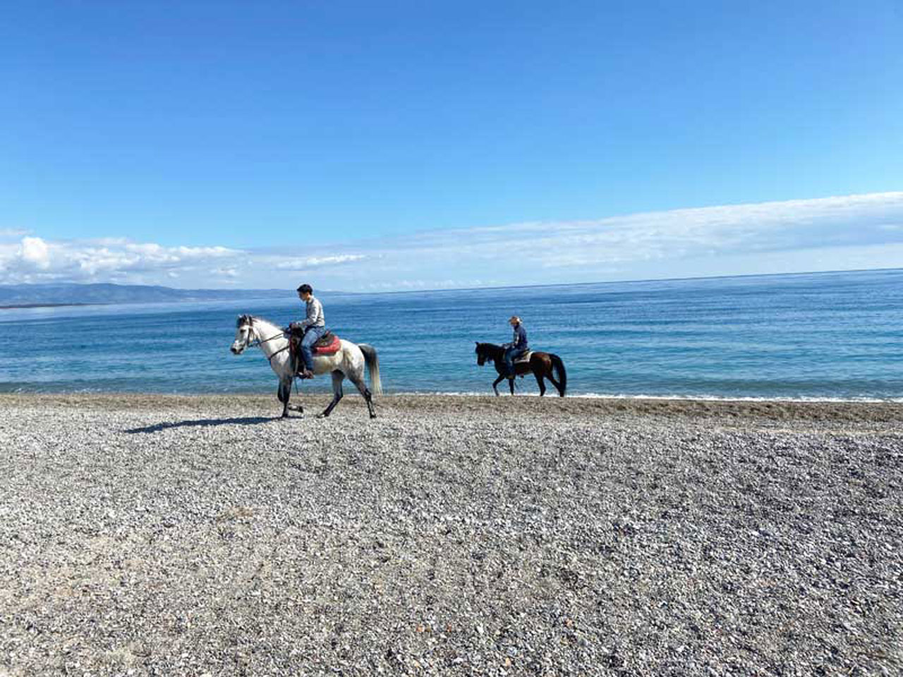 Two riders on the pebble beach by the Ionian Sea