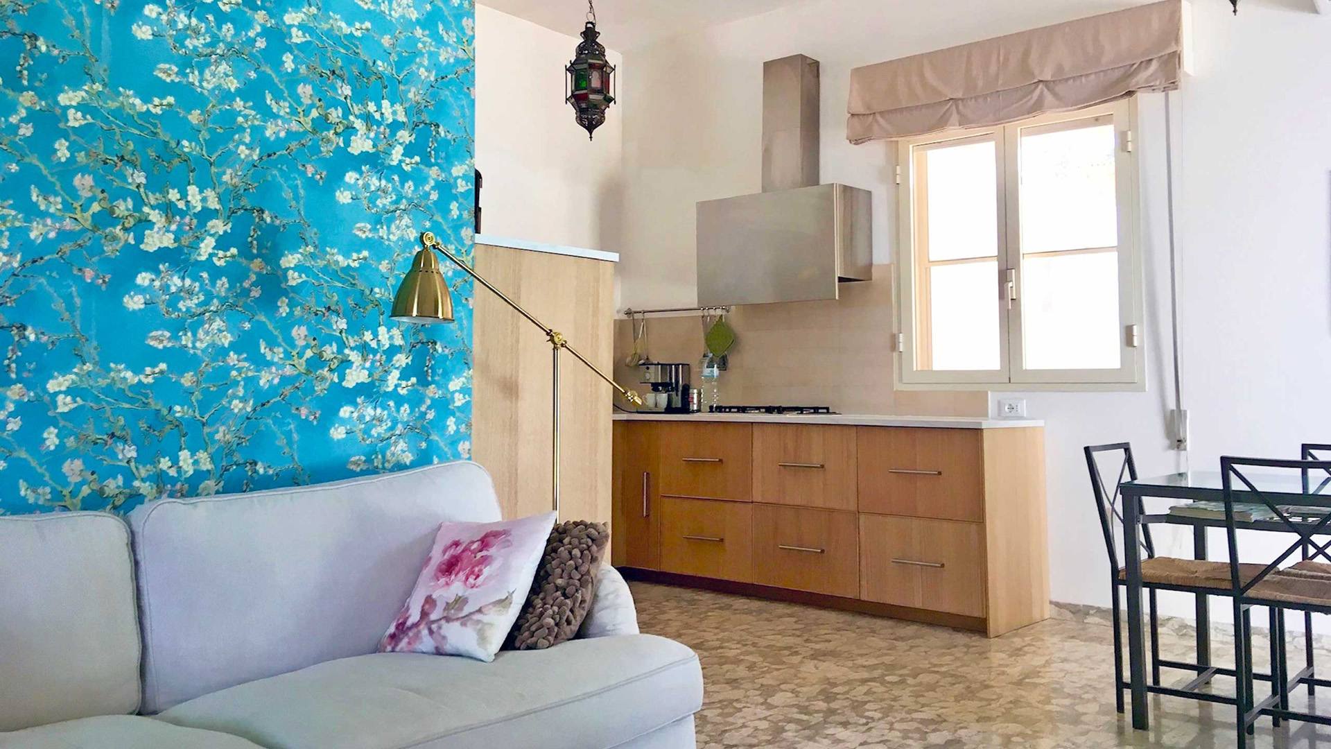 Wohnzimmer mit offener Küche in Villa Gabellotti, mit weißem Sofa und Tapete mit Blütenzweigen