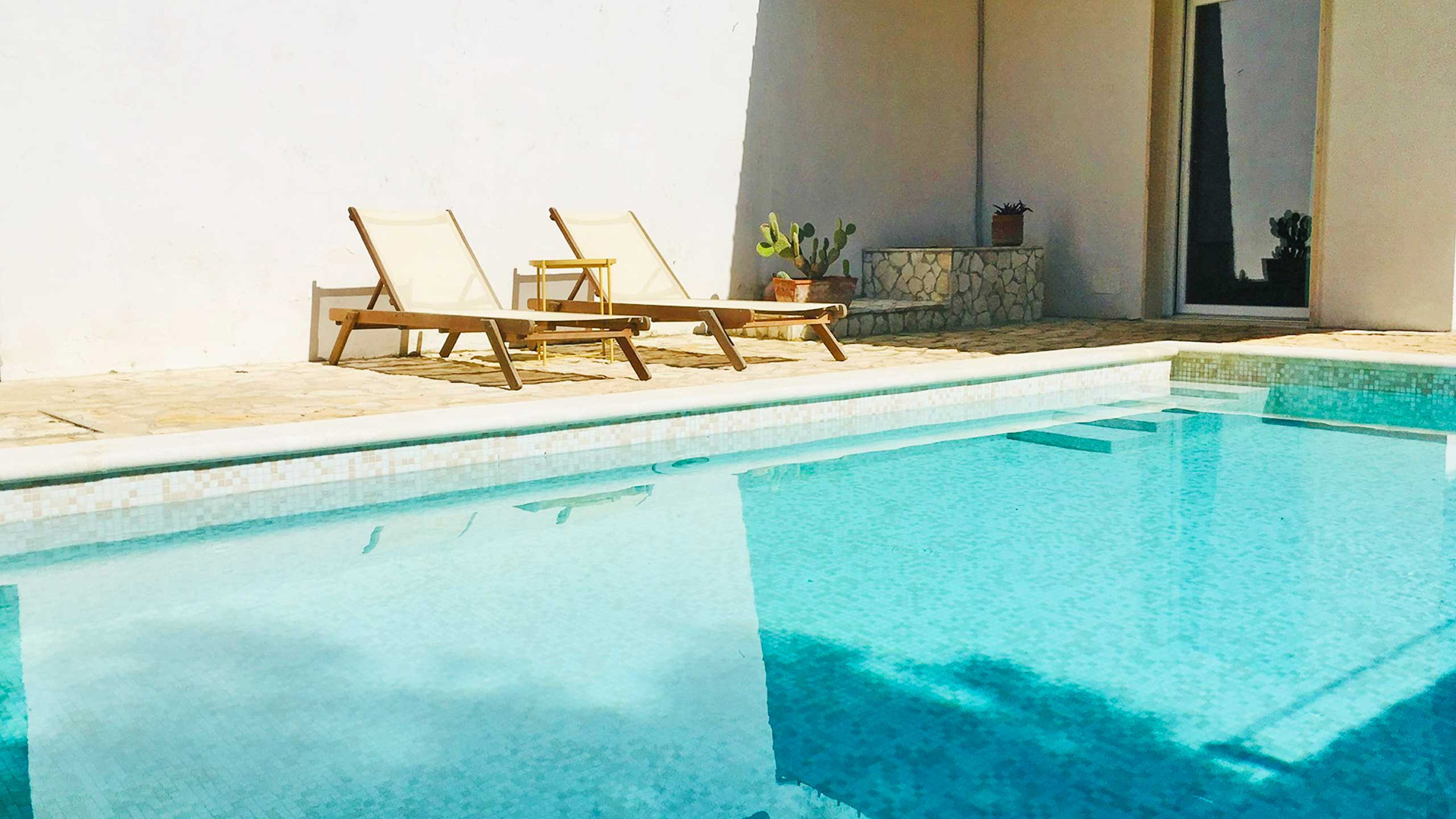Pool von Villa Gabellotti mit zwei hölzernen Liegestühlen an der weißen Mauer