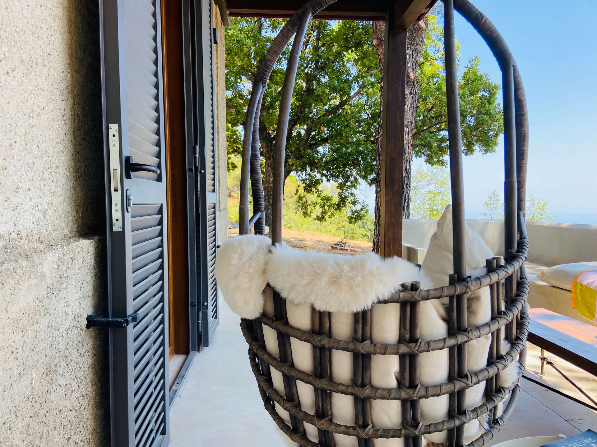 Hangstoel met een schapenvacht op de veranda van Villa Grimiti, met de bomen en de zee in de verte