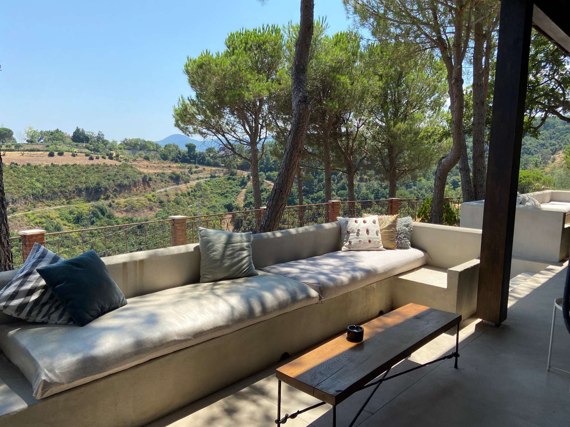 Loungebank met kussens op de veranda van Villa Grimiti, met uitzicht op de beboste heuvels