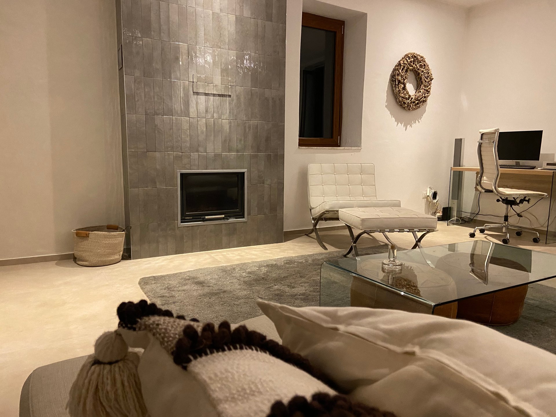 Woonkamer van Villa Grimiti met een haard in een grijs betegelde wand, een witte leren stoel en een werkplek