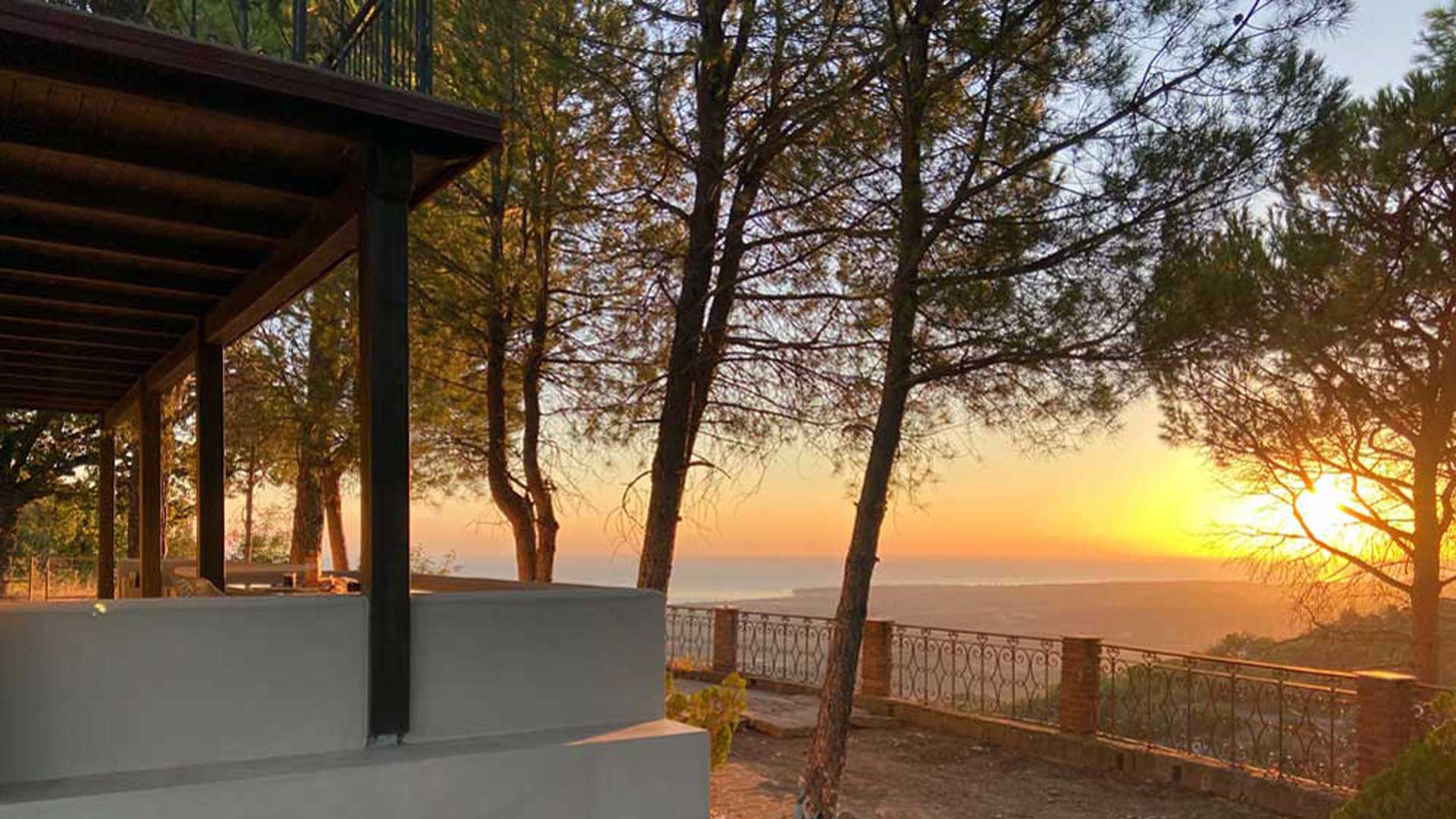 Zonsondergang boven zee, gezien vanaf de veranda van Villa Grimiti tussen de pijnbomen